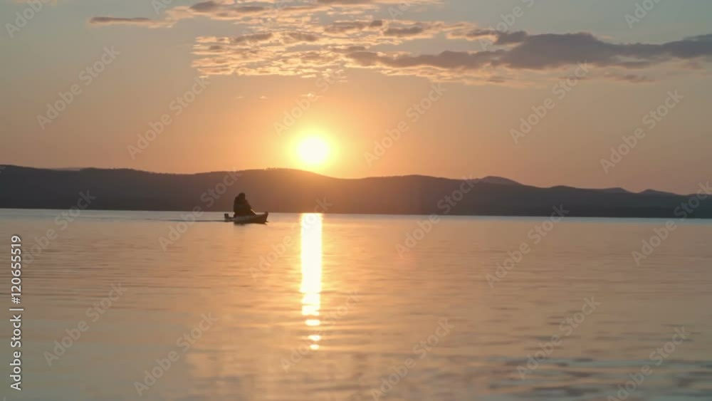 Lockdown of silhouette of tourist slowly paddling kayak across lake under setting sun Lockdown of silhouette of tourist slowly paddling kayak across lake under setting sun