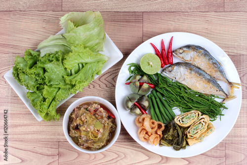 Green chili dip " Nam Prik Num" and dish of deep fired mackarelss,vegetable omelet,crispy pork rind,pickle lettuce,halve green lemon,red chili and boiled of eggplant,lentils,acacia on wood. Top view