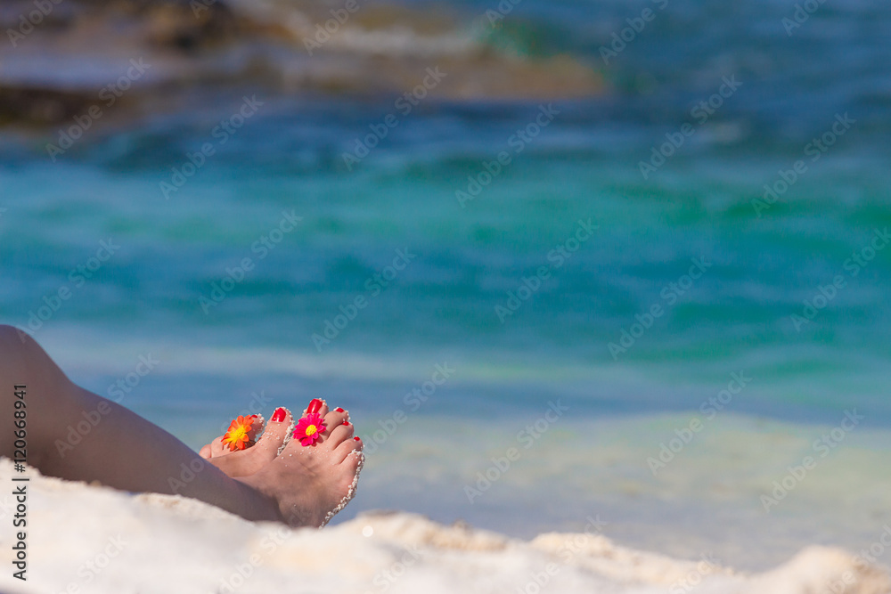 Beautiful female legs with flower decoration on sandy beach. Blue ocean and waves in the background. Travel and summer vacation concepts. Space for copy. Beautiful female legs with flower decoration on sandy beach. Blue ocean and waves in the background. Travel and summer vacation concepts. Space for copy.