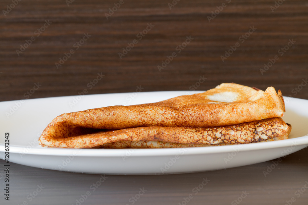 One traditional russian pancake folded triangle on a white plate on the dark background One traditional russian pancake folded triangle on a white plate on the dark background