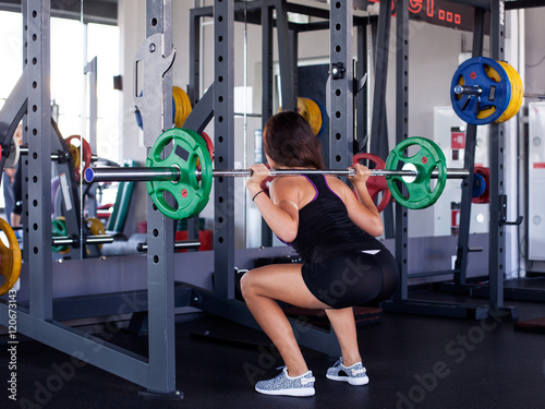 Young athletic woman squatting with a barbell on the shoulders at the gym