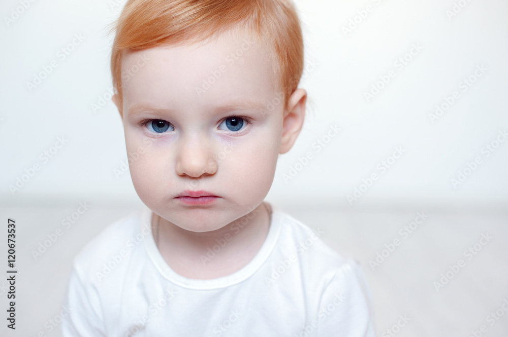 Red-haired child with big blue eyes against a white wall with copyspace Red-haired child with big blue eyes against a white wall with copyspace