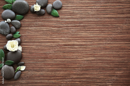 Spa stones with rose and petals on wooden background