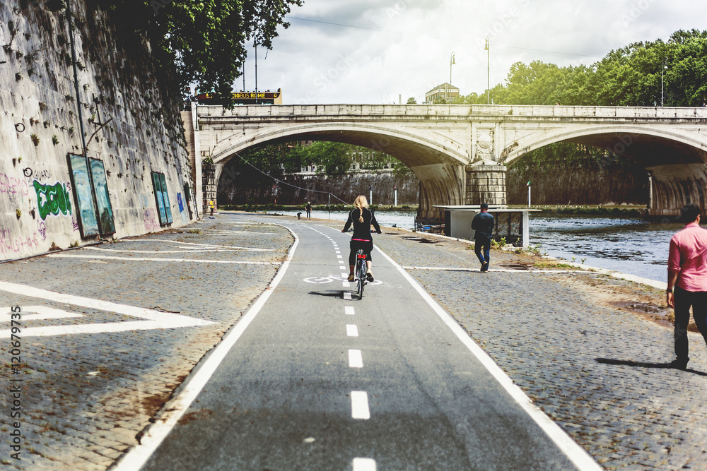 Naklejka premium Girl riding a bike over a bike path in lungotevere, close to Tiber river. Rome, Italy.