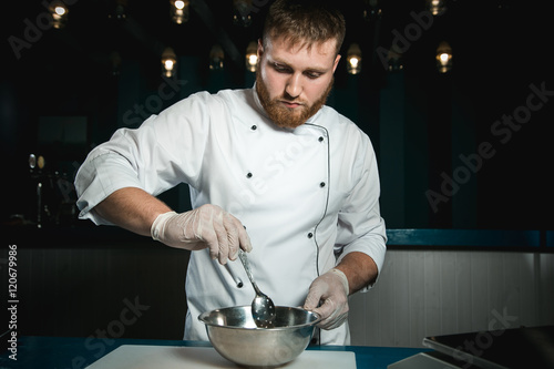 Cheerful bearded chef cook cooking while cooking meals in the kitchen