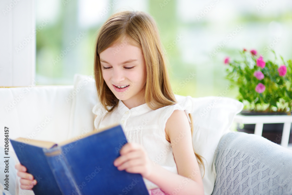 Adorable little girl reading a book in white living room Adorable little girl reading a book in white living room