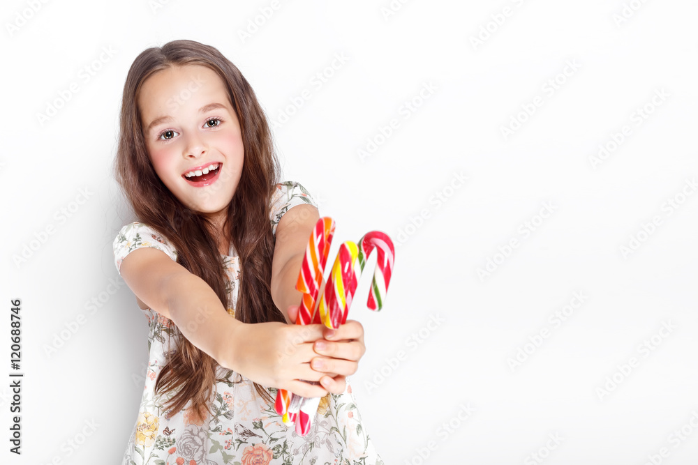 Happy, smiling cute little girl eating cristmas candy cane. Posing against a white wall. Happy, smiling cute little girl eating cristmas candy cane. Posing against a white wall.