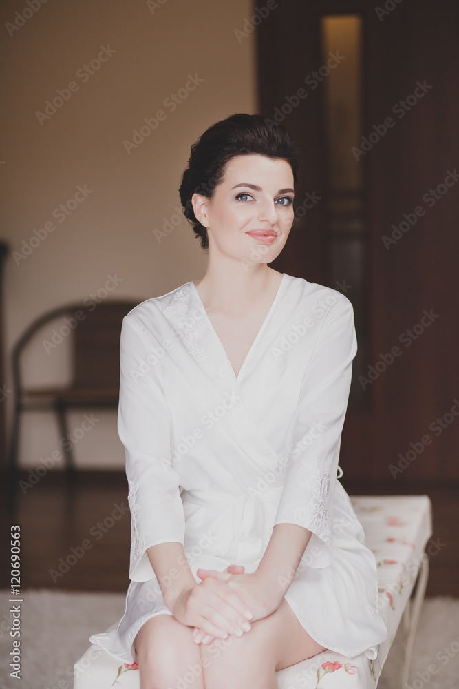 Woman dressed in white bathrobe stands near window Woman dressed in white bathrobe stands near window