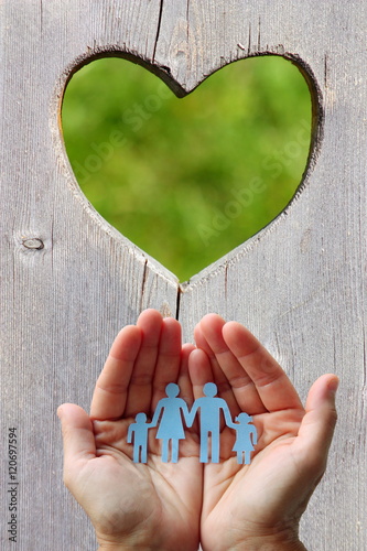 Paper family in hands on wooden background with heart 
