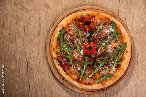 Pizza with meat and arugula served on wooden board