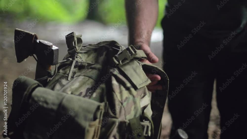 A male hiker puts on a backpack in slow motion. He’s strong and rugged with a beard.