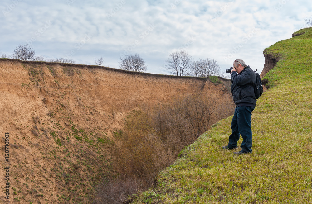 Mature photographer taking photo standing on the edge of ravine at spring season