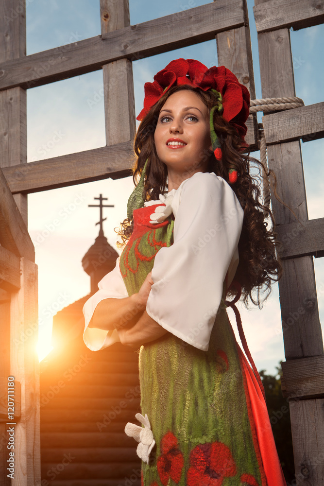 Young woman in Russian traditional dress is standing near wooden