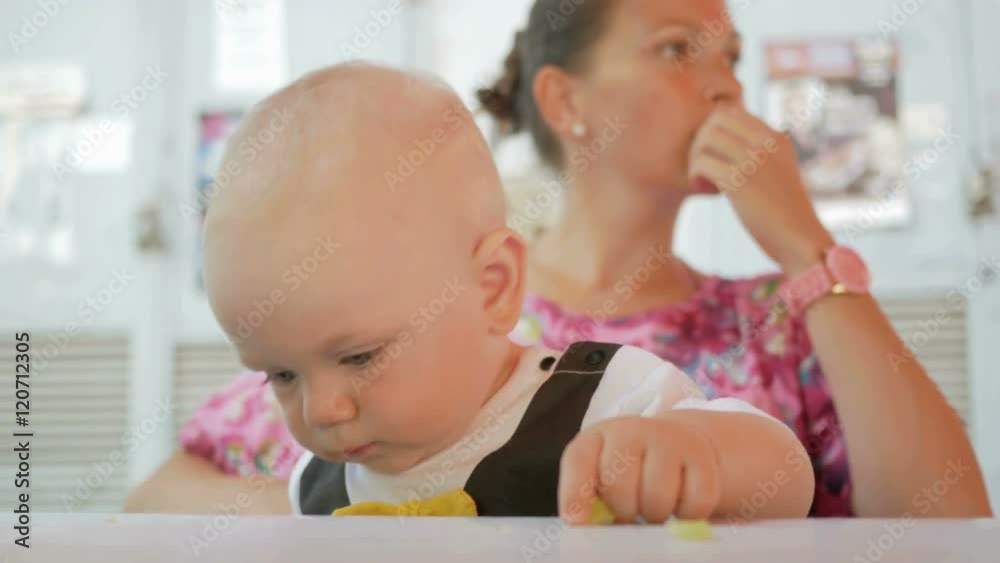Mom and baby in a beautiful dress with butterfly eat in a cafe on the street. Kid eating a piece of cucumber salad mother Mom and baby in a beautiful dress with butterfly eat in a cafe on the street. Kid eating a piece of cucumber salad mother