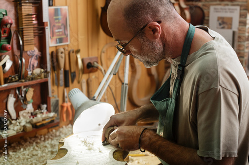 Violin maker carving and cutting on wooden corpus for new instru photo