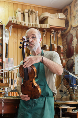 Instrument maker in his workshop checking finished violin