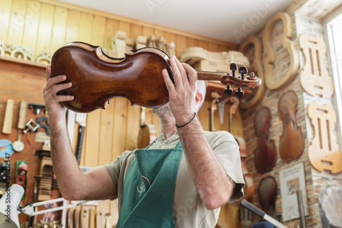 Violin maker checking finished instrument to his satisfaction photo