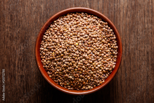 Rustic ceramic bowl of uncooked lentils isolated on dark wood from above
