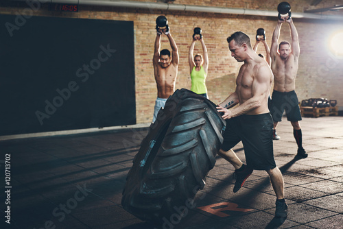 Muscular shirtless man moving large tire