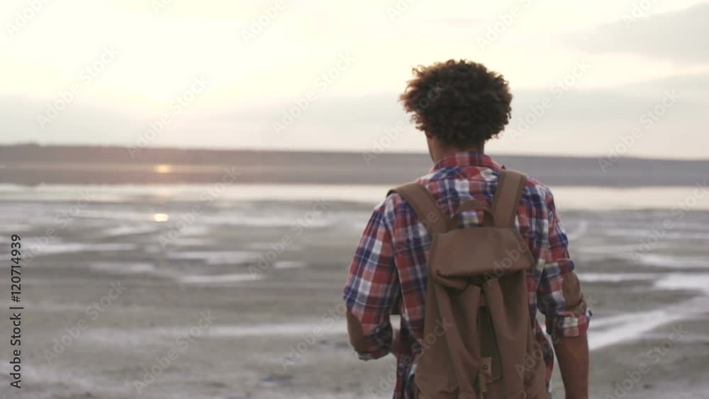 Back view of an afro american traveler man walking at the beach watching sunset Back view of an afro american traveler man walking at the beach watching sunset