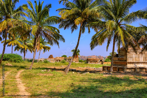 Tourist indian landmark Ancient ruins in Hampi, India. Beautiful nature scenery with a path along the ruins, bright blue sky and palm trees