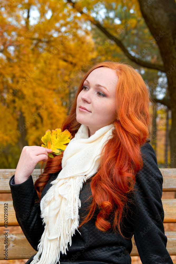 beautiful young girl portrait sit on bench in park with yellow leaf in hand, fall season, redhead, long hair