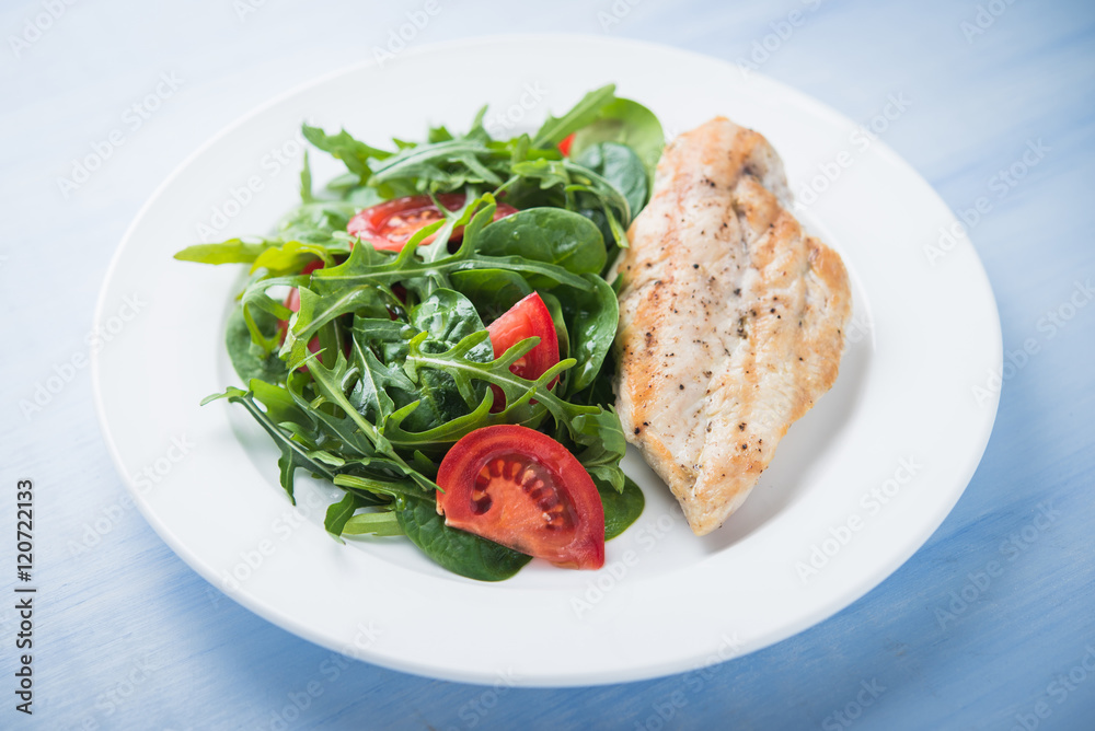Roasted chicken breast and fresh salad with tomato and greens (spinach, arugula) close up on blue wooden background. Healthy food. Roasted chicken breast and fresh salad with tomato and greens (spinach, arugula) close up on blue wooden background. Healthy food.