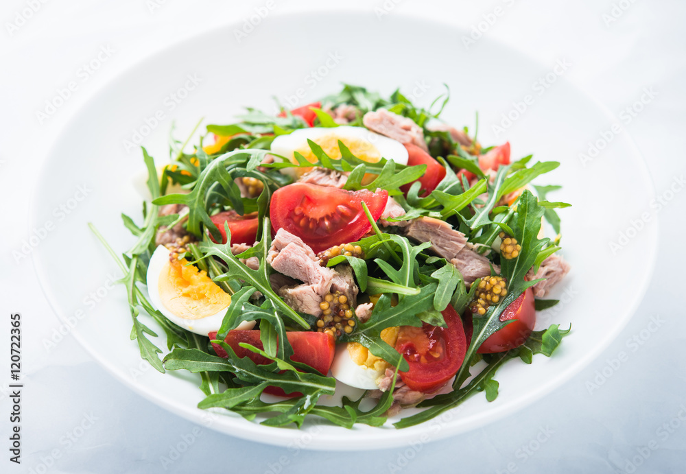 Fresh salad with tuna, tomatoes, eggs, arugula and mustard on white textured background close up. Healthy food. Fresh salad with tuna, tomatoes, eggs, arugula and mustard on white textured background close up. Healthy food.