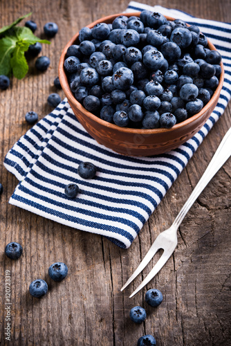 Full bowl of fresh ripe blueberries on old wooden board