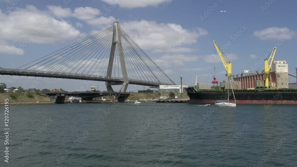 The ANZAC Bridge in Sydney with a sailing boat and airplane passing by with a big cargo ship next to it The ANZAC Bridge in Sydney with a sailing boat and airplane passing by with a big cargo ship next to it