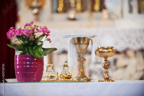 Two golden chalices on the altar with wine, water and violet flowers next to it.