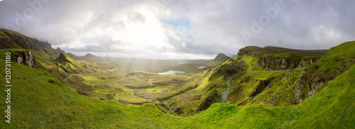 View from the top of Quiraing into the green Valley with it´s ponds. Sun beams breaking through a heavy cloud cover.