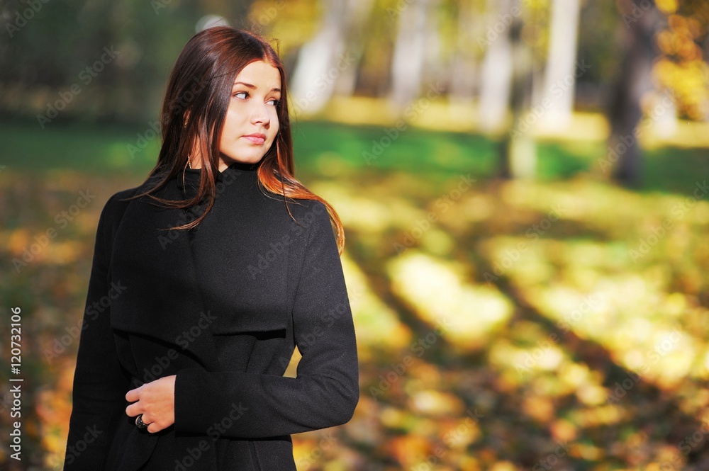 Young beautiful long-haired girl in a black coat cute smiles and looks away in the fall. Young beautiful long-haired girl in a black coat cute smiles and looks away in the fall.