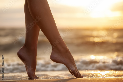 sexy woman's legs  on the sandy  beach with the sea water and su