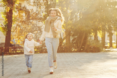 Mother and daughter running through the autumn park.