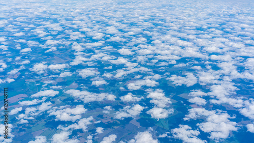 View from airplane's window seeing small groups of clouds scattering and floating in the blue sky like cottons above Russia's land covering with clouds' shadow in some parts of the landscape