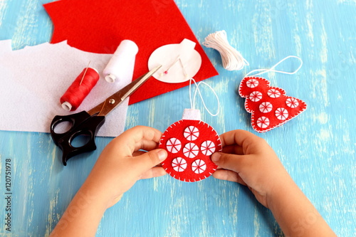 Child holding a Christmas ball in his hands. Child shows Christmas ball. Christmas tree crafts, scissors, thread, needles, felt scraps on a blue background. Sewing concept