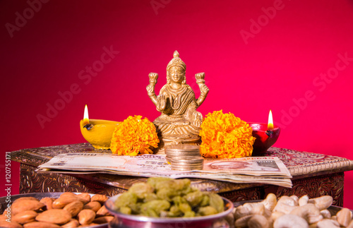 oil lamp or diya with crackers, sweet or mithai, dry fruits, indian currency notes, marigold flower and statue of Goddess Laxmi on diwali night while laxmi pujan or pooja
