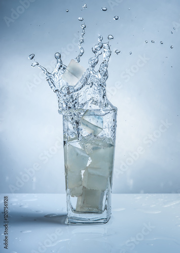 Ice cubes with water splash in glasses on blue background