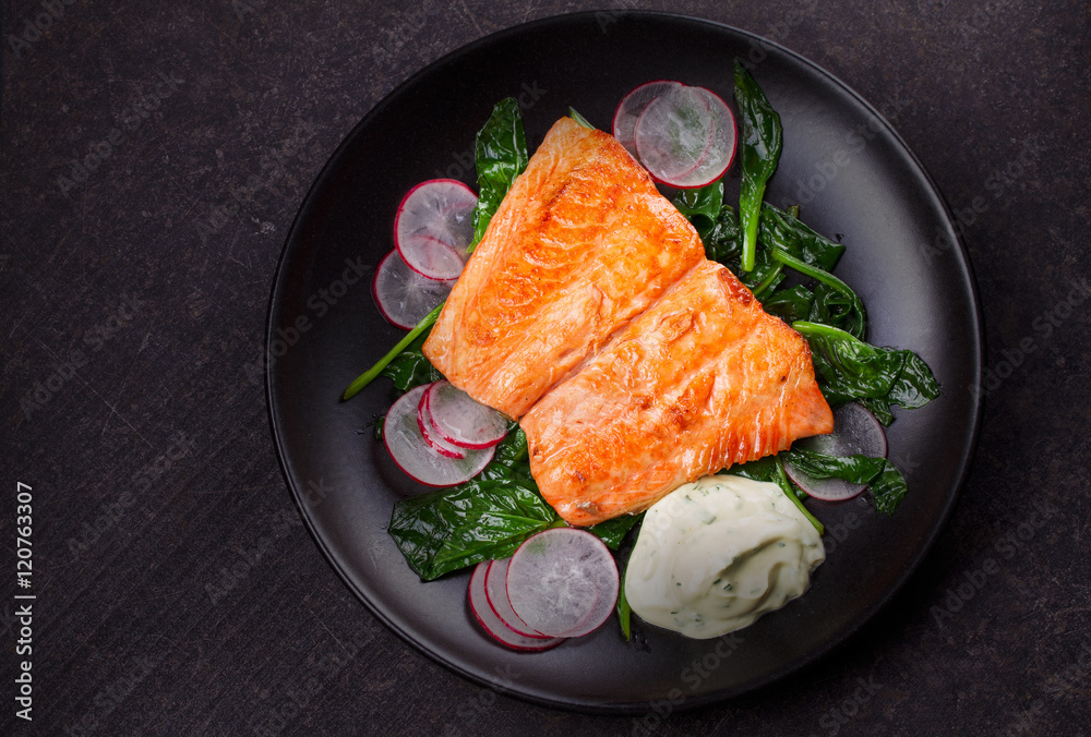 Broiled salmon with radish and spinach, served on black plate. View from above, top studio shot Broiled salmon with radish and spinach, served on black plate. View from above, top studio shot