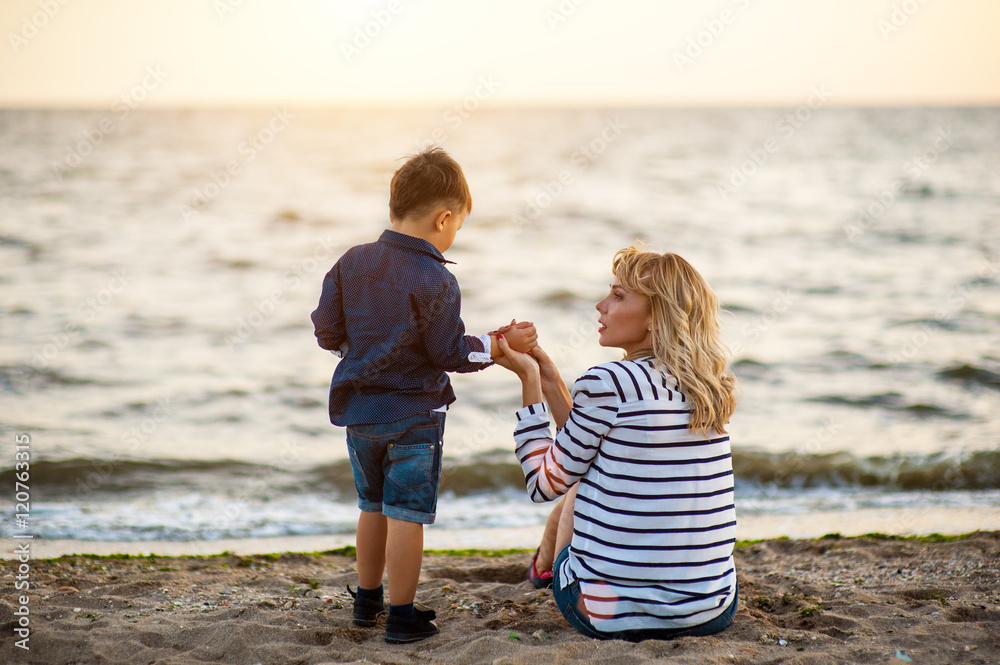 Beautiful woman with a child of four years playing on the beach near the sea Beautiful woman with a child of four years playing on the beach near the sea