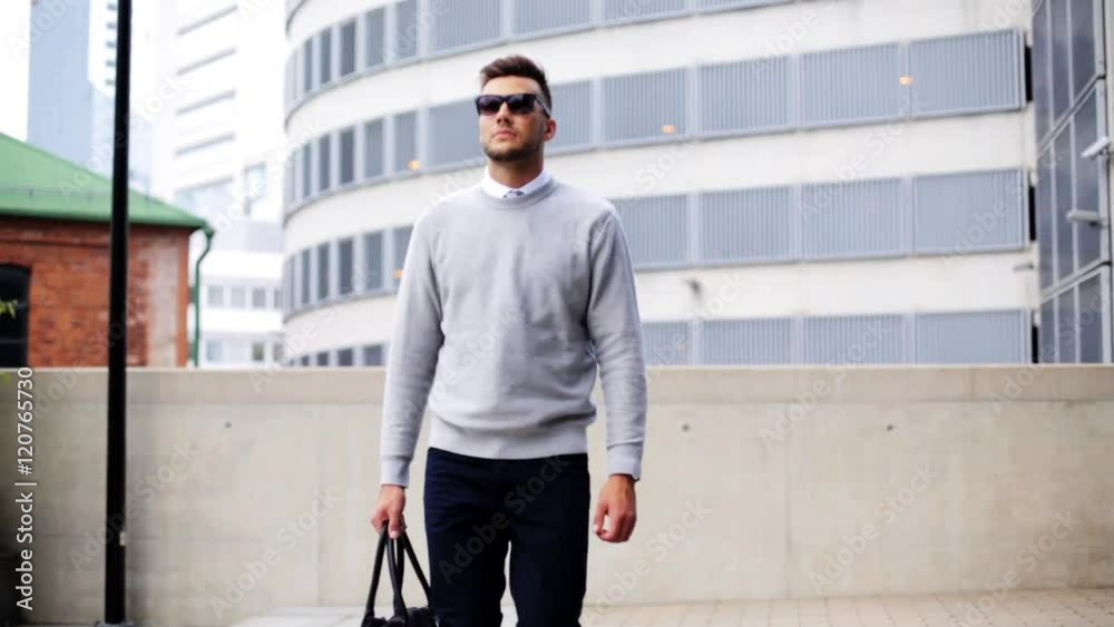 young man with sunglasses and bag walking in city