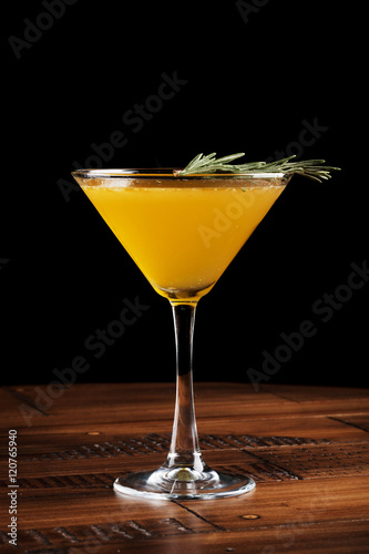 Orange alcohol cocktail in a glass on a wooden surface. Black background.