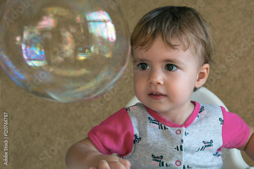 clouse-up portrait two-year girl inflates a large circular bubble