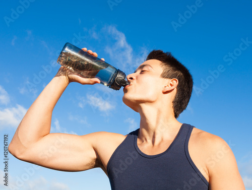 Fit male athlete drinking bottle of water. 