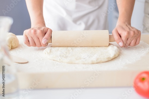 Woman rolling pizza dough using rolling pin.
