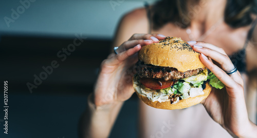 Young girl holding in female hands fast food burger, american unhealthy calories meal on background, mockup with copy space for text message or design, hungry human with grilled hamburger front view