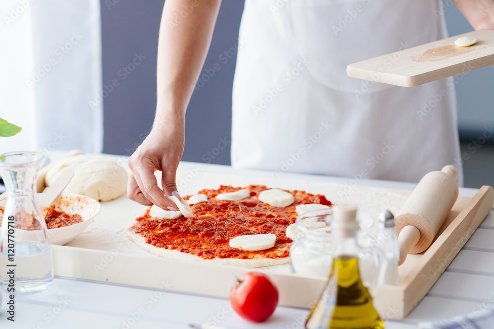 Woman puts slices of mozzarella on the pizza Woman puts slices of mozzarella on the pizza