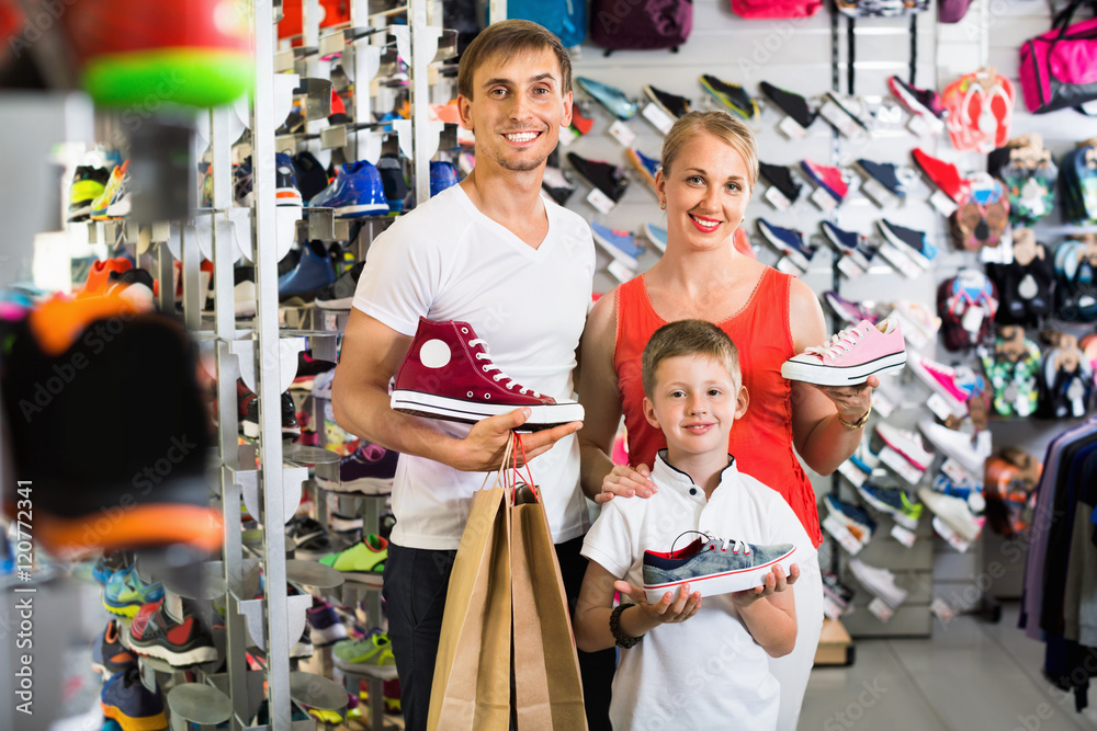 Cheerful young parents with boy in school age shopping shoes