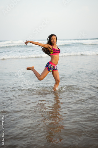 Black sporty woman dancing at the beach into the sea. Playful brazilian dancer splashing water.